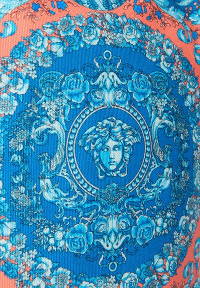 Μπλε και κοραλλί ύφασμα με περίτεχνο ανθισμένο σχέδιο που περιβάλλει ένα κεντρικό έμβλημα κεφαλής Μέδουσας σε κυκλικό πλαίσιο.