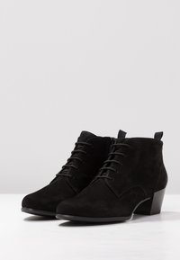Botas de tobillo de ante negro con punta redondeada, parte delantera con cordones y un pequeño tacón cuadrado. La cremallera lateral y los detalles de costura añaden textura al diseño.