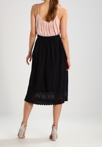 Jupe noire avec bord en dentelle à l'ourlet, assortie à un haut rose. Tissu léger, longueur genou, portée avec des chaussures à talons beiges.