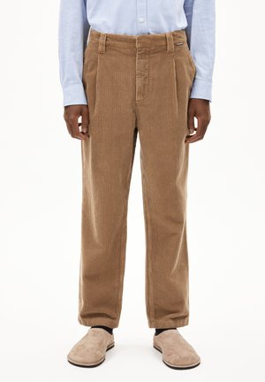 Brown corduroy trousers featuring front pleats, a relaxed fit, and a textured finish. Paired with a light blue shirt and beige slippers.