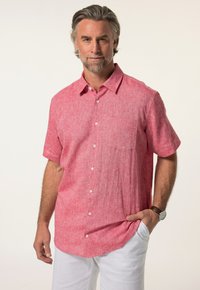 Camicetta a maniche corte con colletto in tessuto rosso chiaro a trama; presenta una tasca sul petto e chiusura con bottoni, abbinata a pantaloni bianchi.