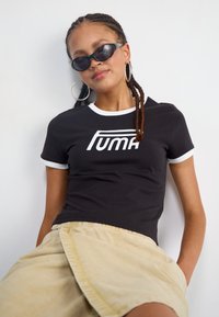 Tricou scurt negru cu mânecă scurtă, cu margine albă, având un logo mare alb "PUMA". Purtați cu o fustă bej.
