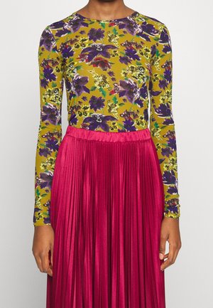 Personne portant un haut jaune à manches longues avec un imprimé floral violet et une jupe plissée rose vif taille haute.