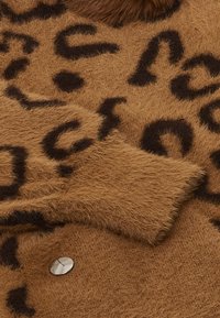 Hnědá, načechraná látka svetru s leopardím vzorem v tmavě hnědé barvě. Obsahuje stříbrný knoflíkový akcent na jedné straně.