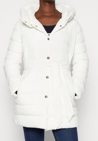 Chaqueta acolchada blanca tipo puffer con capucha, cintura ajustada, botones metálicos y bolsillos laterales, con una tela lisa y texturizada.