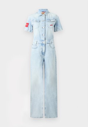 Combinaison en denim bleu clair à manches courtes, boutonnée devant, col, deux poches poitrine, poches latérales, et patches rouges sur la poitrine gauche et la manche.