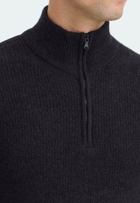 Dunkelgrauer Quarter-Zip-Pullover aus strukturiertem Strickmaterial mit hohem Kragen. Verfügt über einen schwarzen Reißverschluss und gerippte Bündchen.
