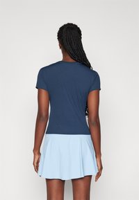 T-shirt aderente blu navy a maniche corte, abbinato a una gonna svasata azzurra, che mette in risalto una texture di tessuto liscia e un design semplice.