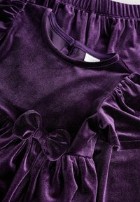 Purple velvet dress with gathered sleeves, a round neckline, and a front bow detail. The texture is soft and plush, suitable for children.
