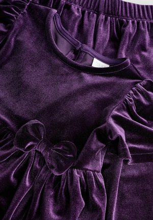 Rochie din catifea purpurie cu mâneci pliate, decolteu rotund și detaliu cu fundă în față. Textura este moale și pufoasă, potrivită pentru copii.