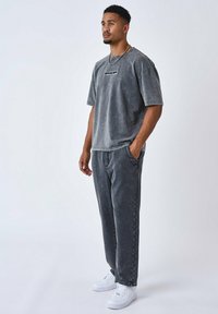 Camiseta de algodón gris con cuello redondo y manga corta, combinada con pantalones de chándal grises a juego. Zapatillas blancas completan el atuendo.