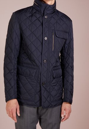 Navy quilted jacket with a high collar, front button closure, and zippered chest pocket. Features two side pockets and a textured design.
