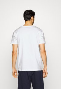 Hvit kortermet t-skjorte vist fra baksiden, laget av bomull, med et rent design og rund hals. Ledig passform.