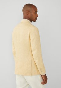 Blazer de lino amarillo claro con un ajuste entallado, ventizo trasero y puños abotonados. Presenta un acabado suave y texturizado.