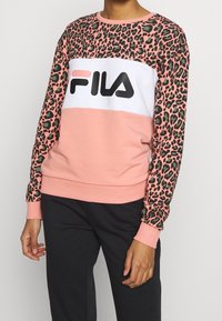 Felpa rosa con maniche a stampa leopardata, banda centrale bianca con il logo "FILA" in nero bold. Polsini e parte inferiore a costine aggiungono texture.