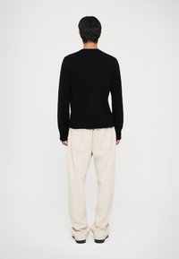 Sort striktrøje med lange ærmer, parret med cremede, afslappede bukser med baglommer. Rent, minimalistisk design.