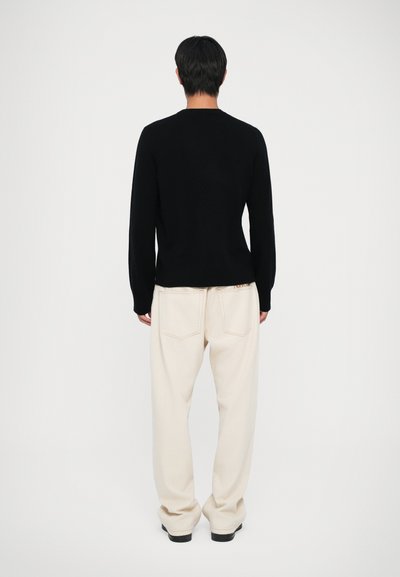 Maglione nero a maglia con maniche lunghe, abbinato a pantaloni crema a vestibilità morbida con tasche posteriori. Design pulito e minimalista.