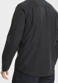 Camicia nera a maniche lunghe realizzata in un tessuto liscio, con colletto classico, polsini con bottone e orlo curvo sul retro.