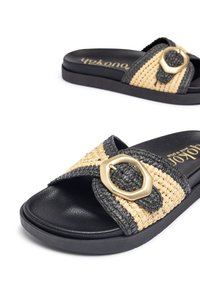 Schwarze und beige geflochtene Riemensandalen mit einem breiten Riemen, der an der Seite mit einer ovalen Schnalle in Goldoptik verziert ist und einer strukturierten schwarzen Sohle ausgestattet ist.
