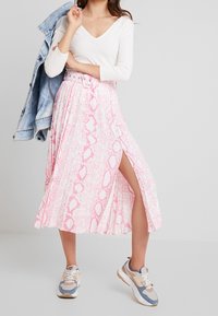 Light pink pleated skirt with a snake print pattern and a thigh-high slit, paired with a white long-sleeve top and chunky sneakers.
