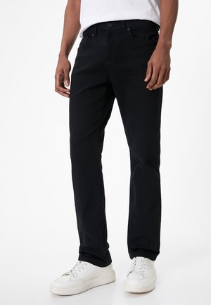 Pantalones de algodón negros con corte recto, diseño de cinco bolsillos y detalles de costura sutiles, combinados con zapatillas blancas.