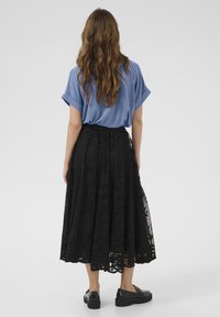 Mėlynas laisvas viršus derinamas su juodu nėriniuotu midi sijonu, kuriame yra gėlių raštai, banguota apatinė dalis ir juodi platforminiai bateliai.