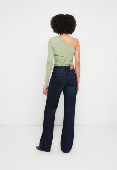Haut asymétrique vert clair à manches longues associé à un jean large taille haute bleu foncé, avec un patch en cuir à l'arrière.