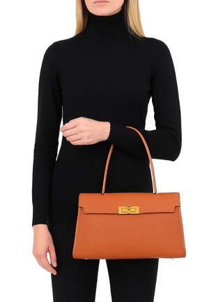 Borsa in pelle tan con un design strutturato, hardware con chiusura in oro e un manico superiore singolo, tenuta nella mano di una modella.