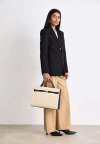 Beige canvas handtas met zwarte accenten en een metalen sluiting, rechthoekige vorm, dubbele handvatten en een gestructureerd ontwerp.