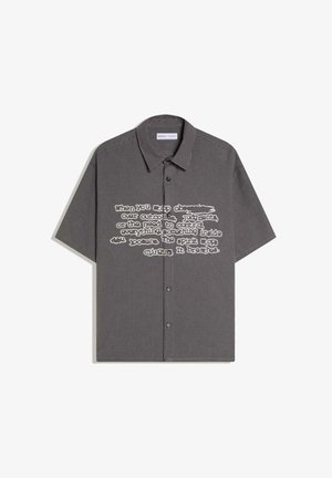 Rövid ujjú, fekete-fehér kockás, gombos ing, fehér nyomtatott szöveggel a mellkason, klasszikus gallérral és két első gombbal.