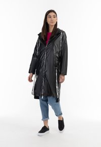 Zwarte lange regenjas met een glanzende afwerking, voorzien van witte "LOVE" zijkanten, een capuchon en een rits. Gecombineerd met opgerolde spijkerbroeken en zwarte sneakers.