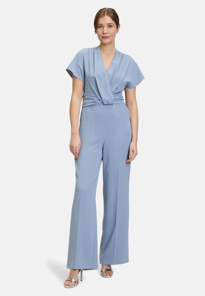 Combinaison bleu clair à manches courtes, décolleté drapé, taille ceinturée et design à jambes larges. Tissu lisse avec des accents minimalistes.