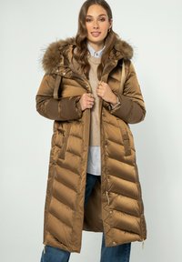 Dlouhá, naducaná hnědá parka s kapucí lemovanou kožešinou, s prošívanými částmi, přední zipem a bočními kapsami. Nosit ji přes lehký svetr a košili.