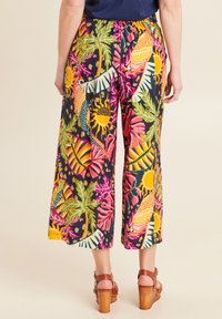 Multikleurige broek met wijde pijpen en een tropisch print met palmbomen, zonnen en levendige patronen. Elastische tailleband, zachte stof, cropped lengte.