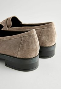 Mocassini in suede color taupe con punta arrotondata e tacco basso. Dettagli di cucitura lungo le cuciture, texture morbida e design minimalista.