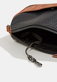 Wnętrze czarnej torebki z teksturowanej skóry z jasnobrązowym suwakiem. Posiada srebrny metalowy suwak i wyściółkę w paski.