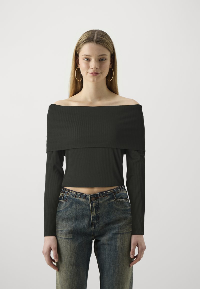 Top corto nero a coste con spalle scoperte e maniche lunghe, abbinato a jeans a vita alta blu sbiaditi con dettagli di bottoni in vita.