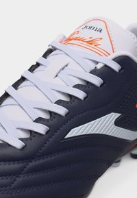 Άσπρο και ναυτικό μπλε ποδοσφαιρικό παπούτσι Joma με άσπρα κορδόνια και πορτοκαλί λογότυπα στη γλώσσα και το πλάι.