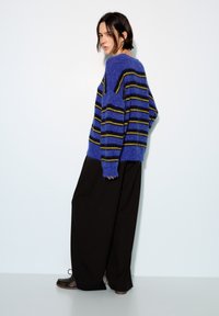 Pull rayé bleu et noir en matière duveteuse, associé à un pantalon large noir. Coupe ample et silhouette décontractée remarquables.