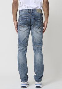 Jeans de mezclilla azul desvanecida con pierna recta, bolsillos traseros con costuras curvas y una etiqueta marrón en la cintura.