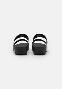 Zwarte sandalen met een eenvoudig ontwerp, bestaande uit twee banden, een platte zool en een textuur in de voetbed. Gemaakt van een flexibel materiaal.