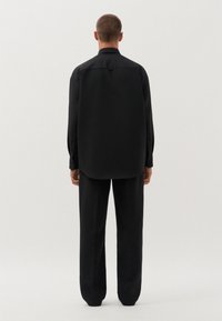 Zwarte overhemd met knopen en bijpassende broek, beide van een gladde stof. Het shirt heeft een gebogen zoom en lange mouwen, met een getailleerde pasvorm.