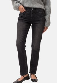 Svarta denimjeans med slim fit, med en glittrande rhinestone-design på midjebandet. Bärs tillsammans med en grå stickad tröja och svarta flats.