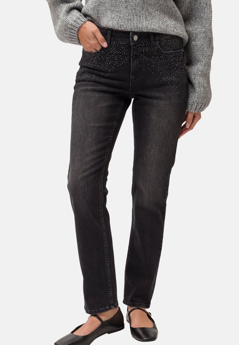 Svarta denimjeans med slim fit, med en glittrande rhinestone-design på midjebandet. Bärs tillsammans med en grå stickad tröja och svarta flats.