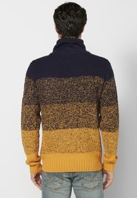 Suéter de punto con un degradado de color que va del azul marino al amarillo mostaza y con un patrón texturizado; cuello alto y puños acanalados en el dobladillo.