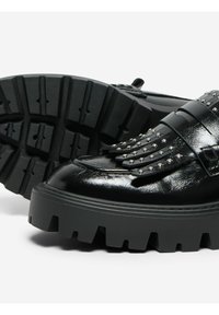 Chaussures en cuir noir avec une semelle épaisse, des détails en franges et des accents cloutés sur le dessus. Semelle texturée et striée pour une meilleure adhérence.