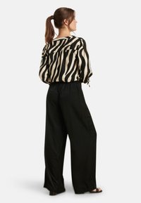 Black and cream long-sleeve blouse with a zebra stripe pattern, paired with loose black pants, featuring a relaxed fit and elastic waistband.
