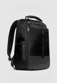 Mochila negra con tejido texturizado, que cuenta con una base de cuero liso, compartimentos con cremallera y una asa superior para transportar.
