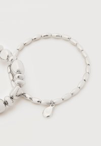 Bracelet en argent avec des liens ovales ornés de perles et un pendentif unique en forme de goutte sur fond blanc.