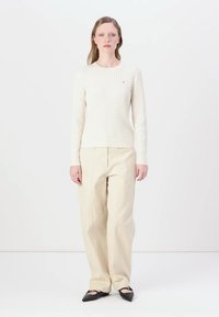 Crème kleurige kabelgebreide trui met lange mouwen, gecombineerd met losse beige broeken en zwarte puntige ballerina's. Eenvoudig ontwerp, geen zichtbare patronen.